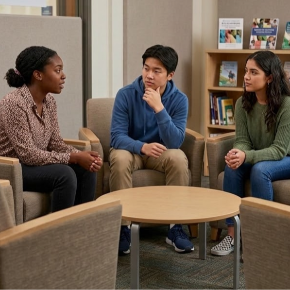 3 students sitting at a table talking.